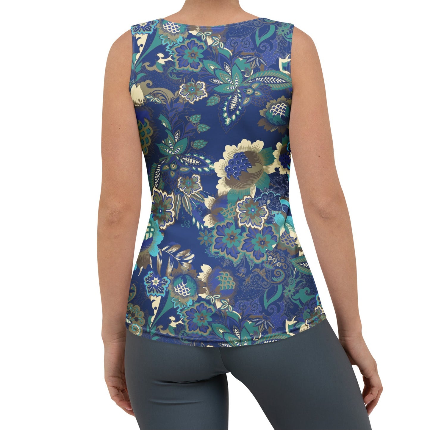 A woman modeling the rio performance tank. a sleeveless athletic tank top with a detailed botanical and floral pattern in navy blue, teal, and gold, paired with dark gray leggings, against a plain white background.