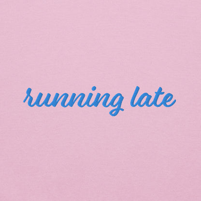 A close-up of The Running Late Sweatshirt, highlighting the "Running Late" embroidery and the iconic heart logo on the sleeve.