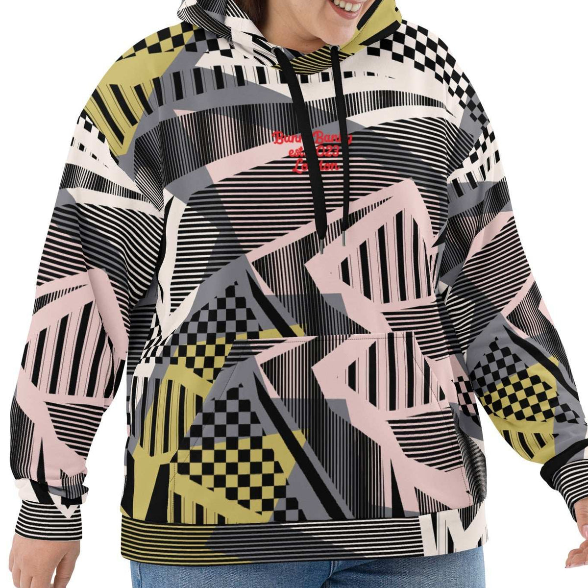 A  model wearing the Sydney Hoodie. The image highlights the Art Deco-inspired pattern of checkers and pinstripes in soft pink, sand, and olive tones, featuring red London branding.