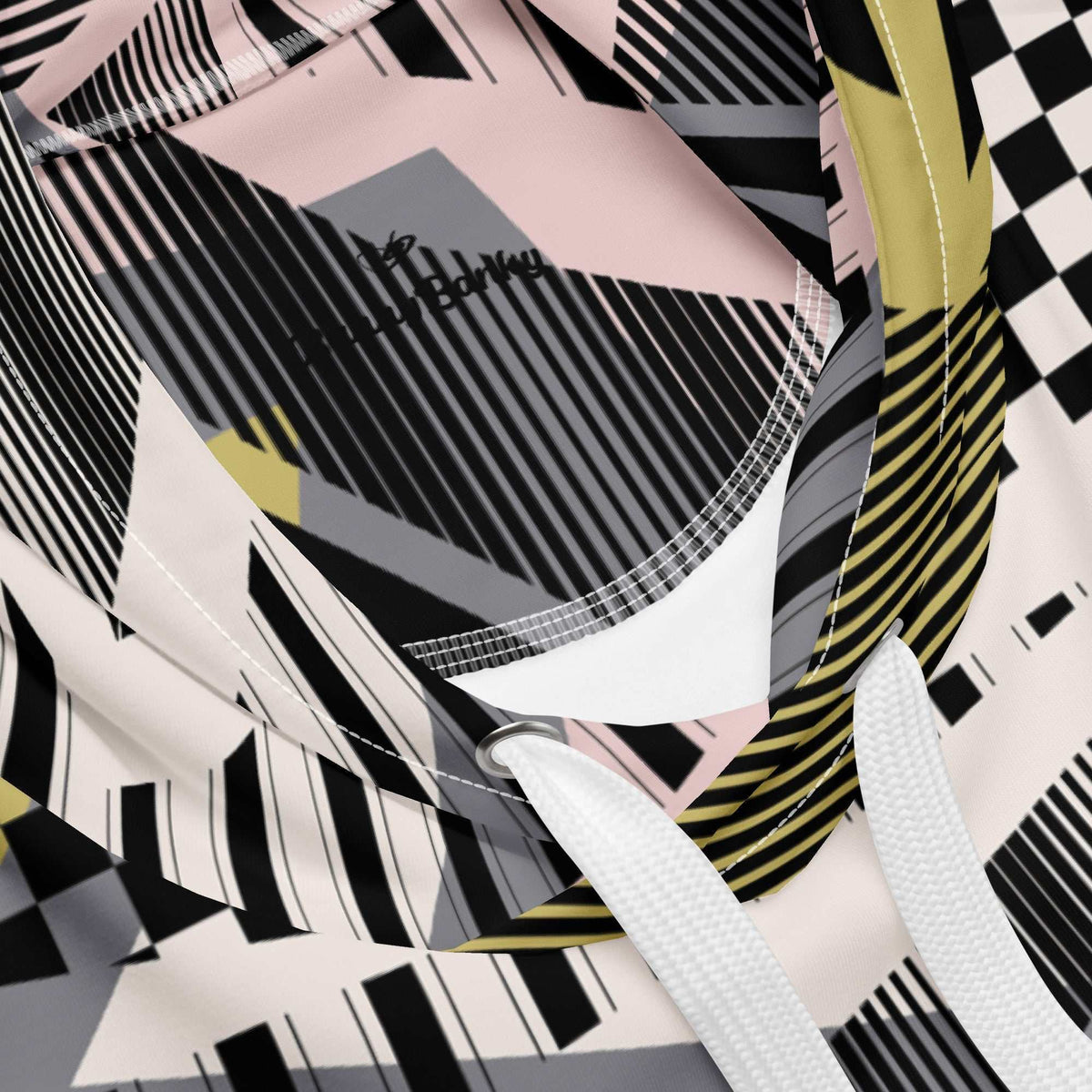 A close up of the Sydney Hoodie. The image highlights the Art Deco-inspired pattern of checkers and pinstripes in soft pink, sand, and olive tones, featuring red London branding.
