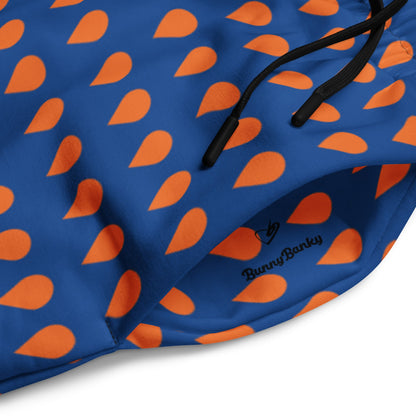 A close up of The Thames Flow Joggers, showing the wide-leg, relaxed silhouette and the orange drop print on the deep navy blue background and the iconic signature inside the pocket in black.