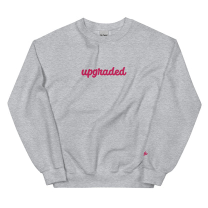 A close-up of The Upgrade Sweatshirt, highlighting the bold "Upgraded" text embroidered in fuschia on the chest, the soft air-jet spun fabric, and the detailed heritage logo print on the back.