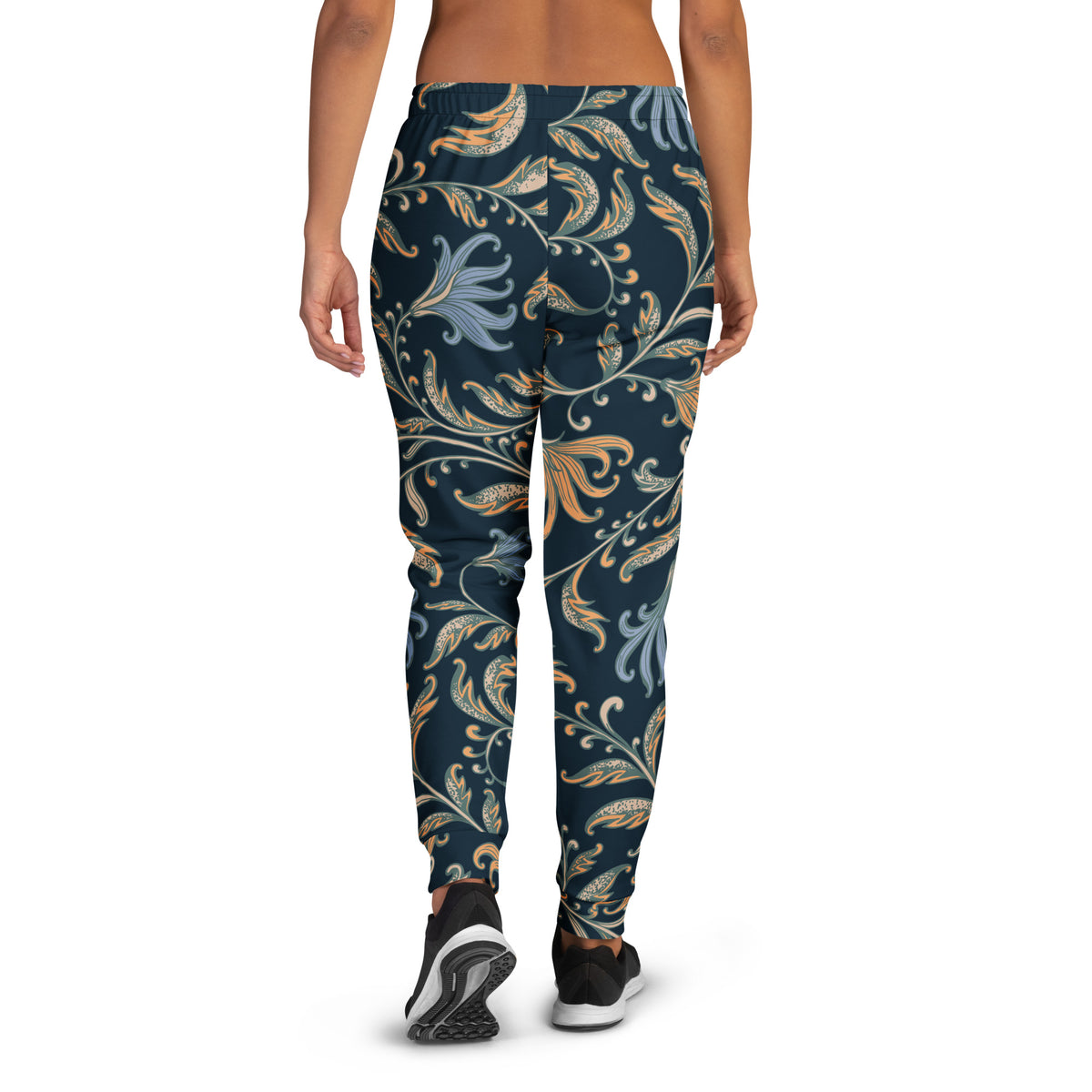 A model wearing the Venice slim fit high-waisted athletic joggers with a dark navy blue background and an intricate botanical pattern in gold, beige, and light blue. The joggers feature a small red logo on the left hip.