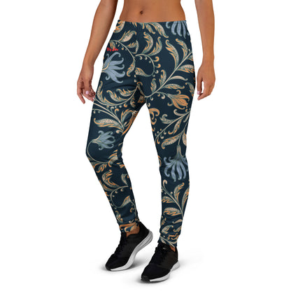 A model wearing the Venice slim fit high-waisted athletic joggers with a dark navy blue background and an intricate botanical pattern in gold, beige, and light blue. The joggers feature a small red logo on the left hip.