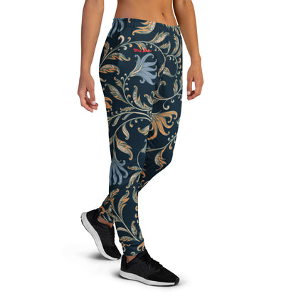 A model wearing the Venice slim fit high-waisted athletic joggers with a dark navy blue background and an intricate botanical pattern in gold, beige, and light blue. The joggers feature a small red logo on the left hip.